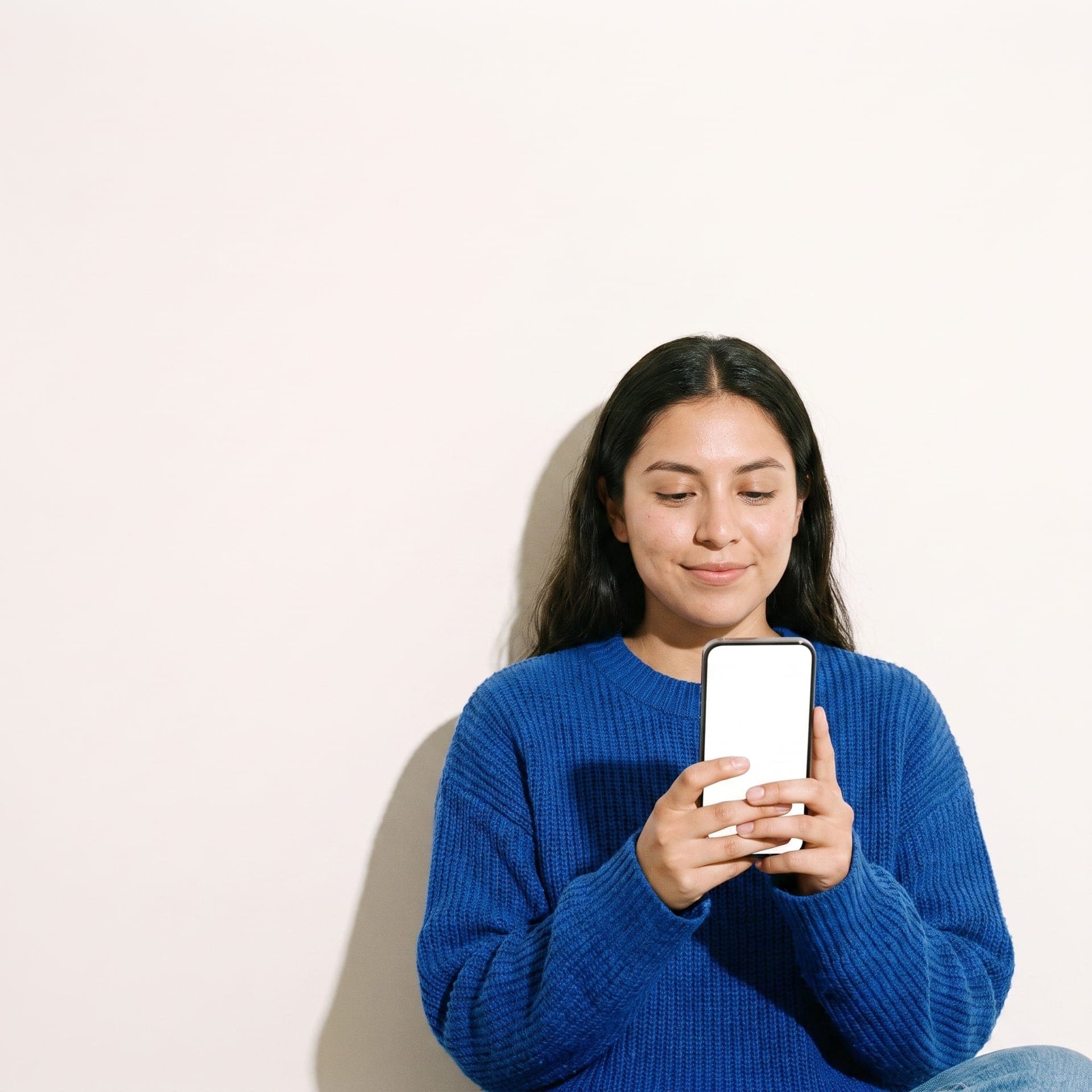 Una mujer con suéter azul mira su teléfono con una sonrisa tranquila